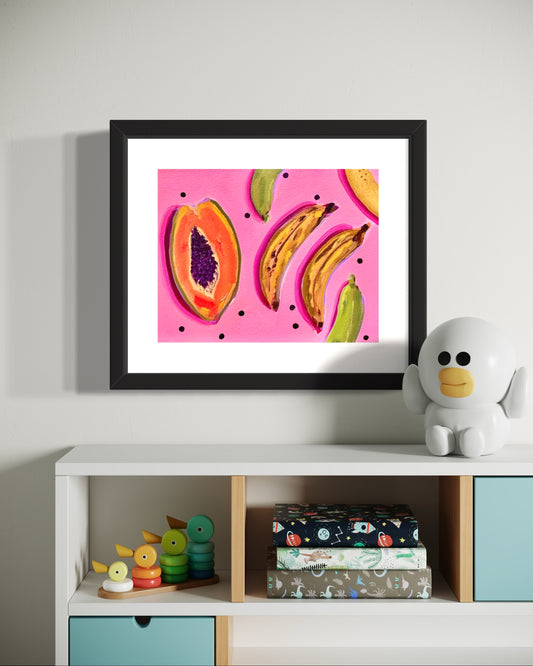 Framed artwork with colorful fruit on a pink background, placed on a shelf with books and toys.