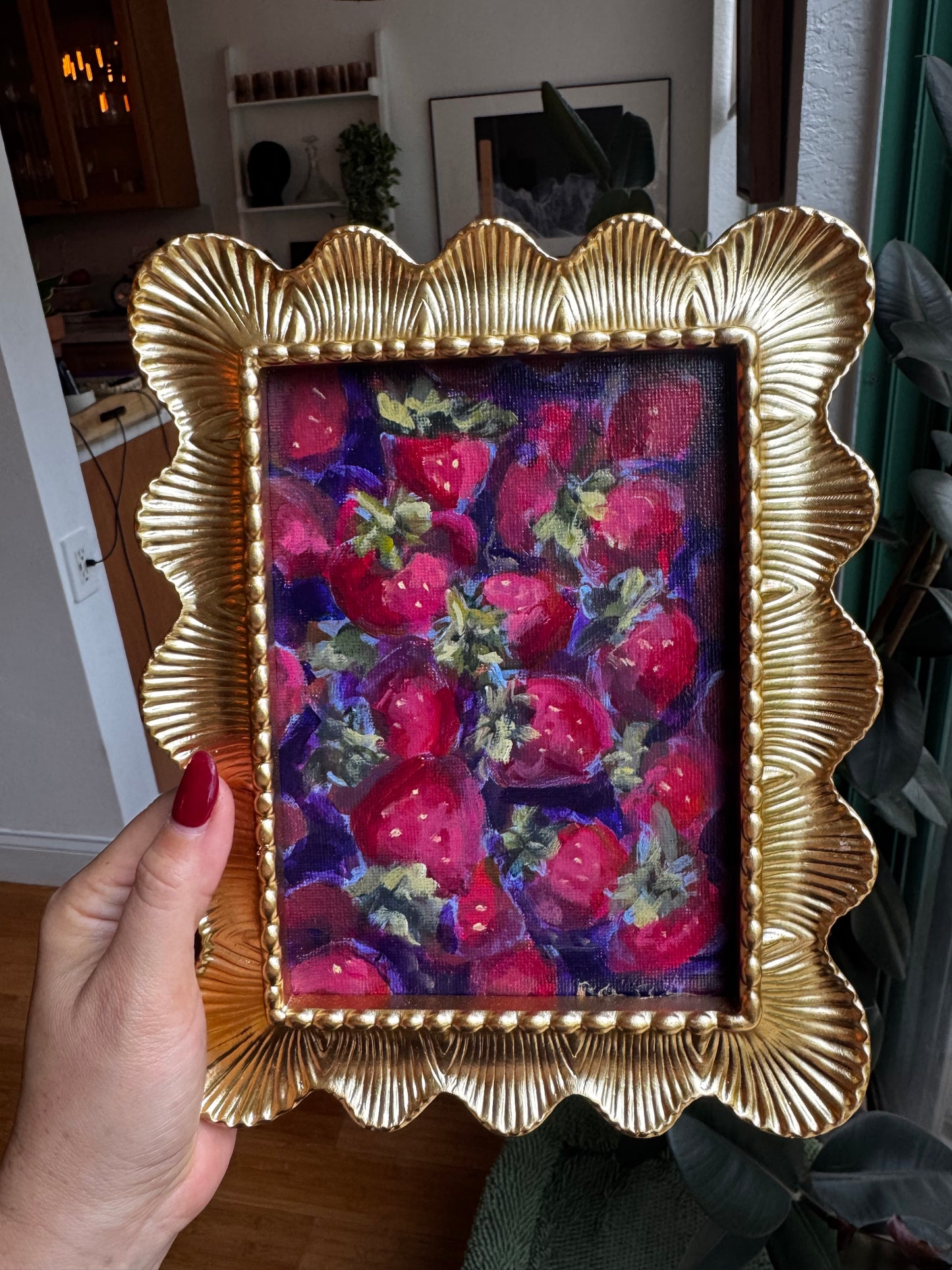 Hand holding a small painting of strawberries in a gold frame.