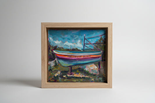 Framed painting of a boat with 'Trebuchet Beach' text, held by a hand.