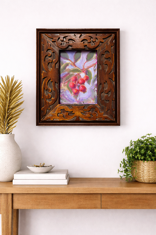 Decorative wooden frame with a painting of berries on a wall above a wooden console table.