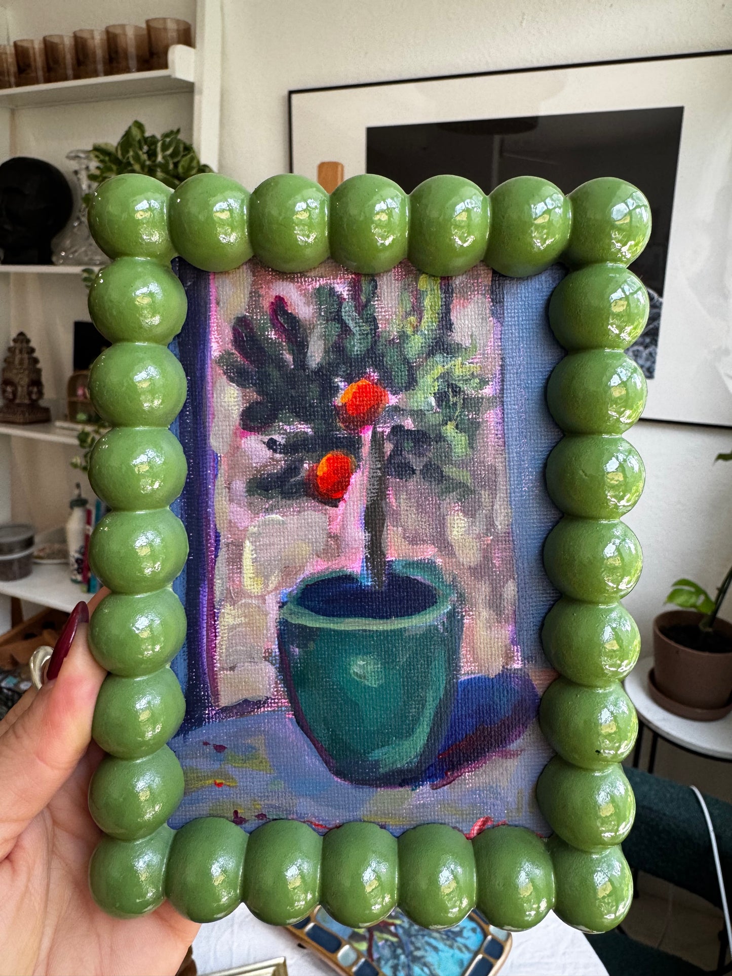 Green beaded frame held over a painting of flowers and a vase.