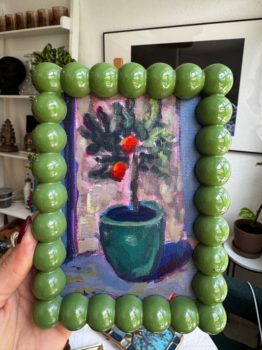Green beaded frame held over a painting of flowers and a vase.