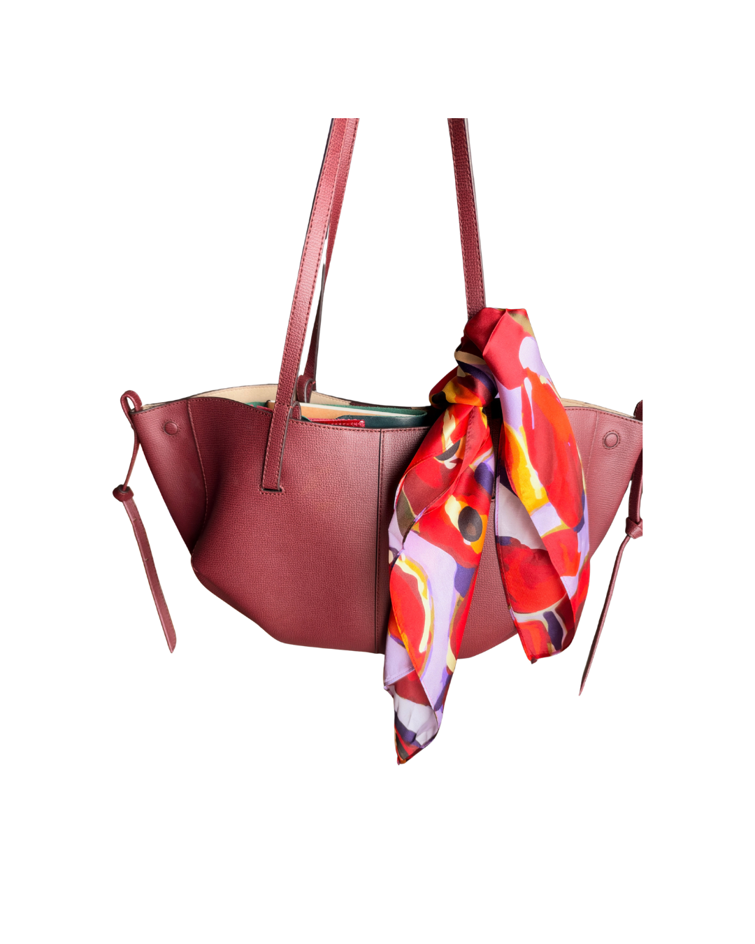 A dusty rose leather tote bag with a vibrant red, orange, and purple abstract patterned scarf tied in a knot and draped over the front, shown against a plain white background.