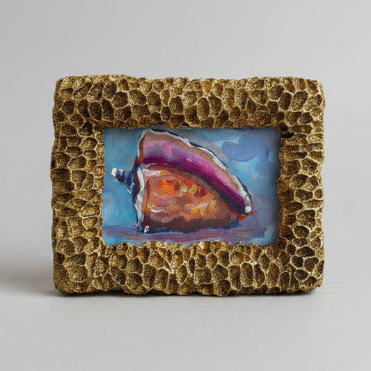 Hand holding a small abstract painting in a textured gold frame with a blurred indoor background.