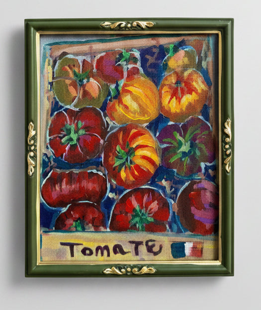 Framed artwork of colorful tomatoes with 'Tomate' label held by a hand.