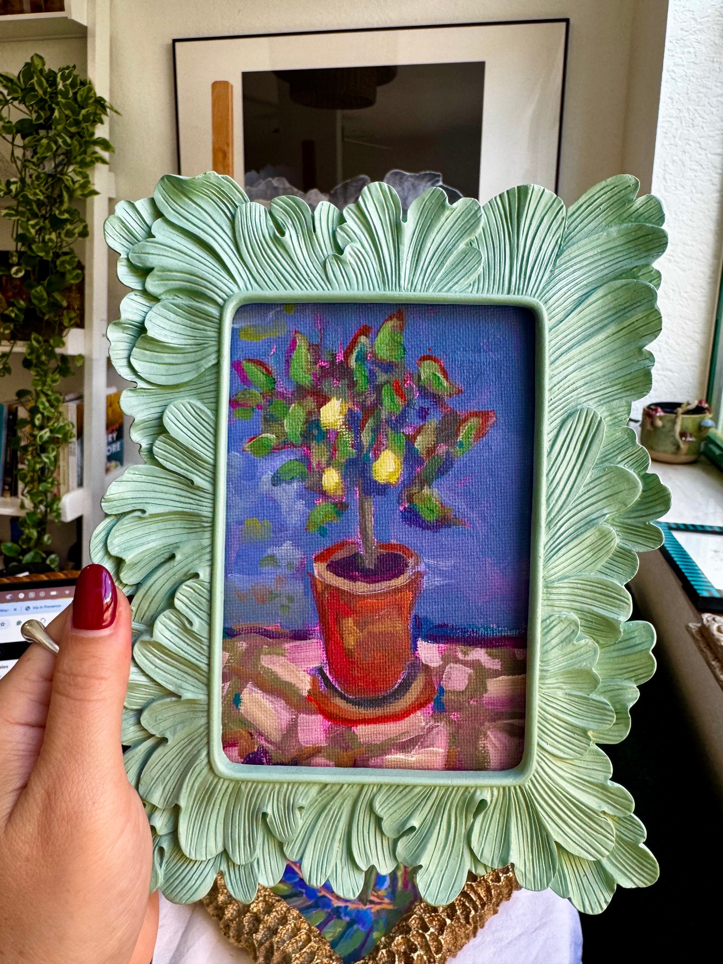 Decorative green frame holding a colorful painting of a potted plant.