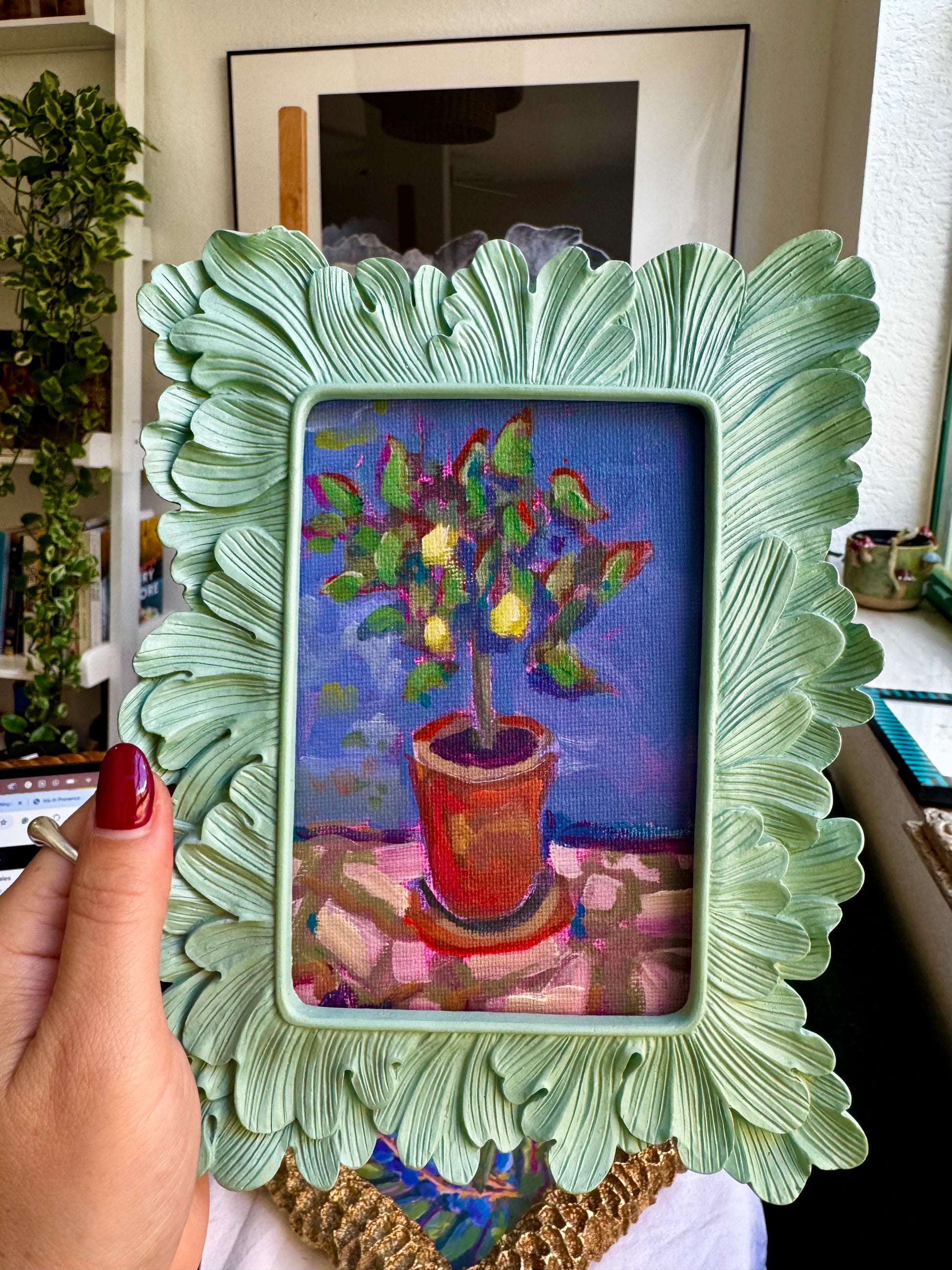 Decorative green frame holding a colorful painting of a potted plant.