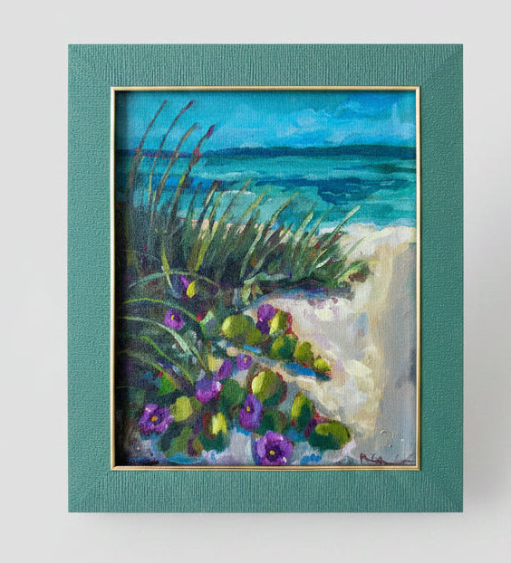 Framed painting of a beach scene with flowers on a white wall