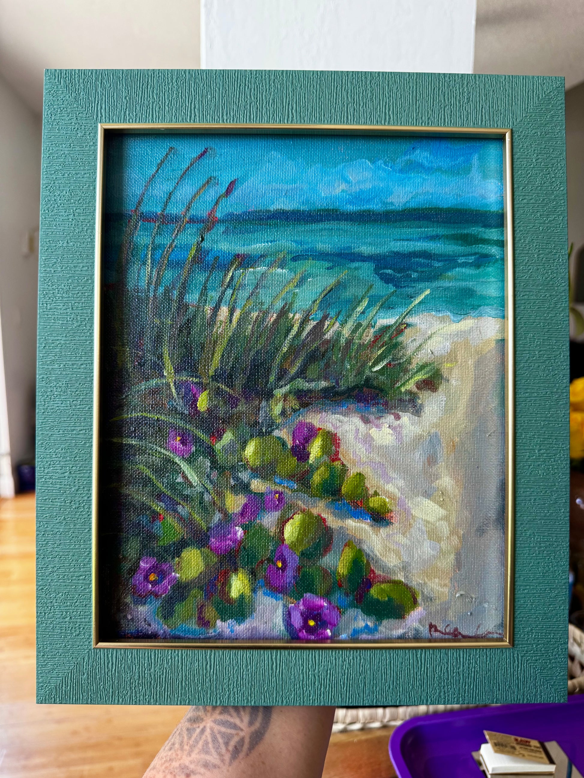 Framed painting of a beach scene with flowers and grass.