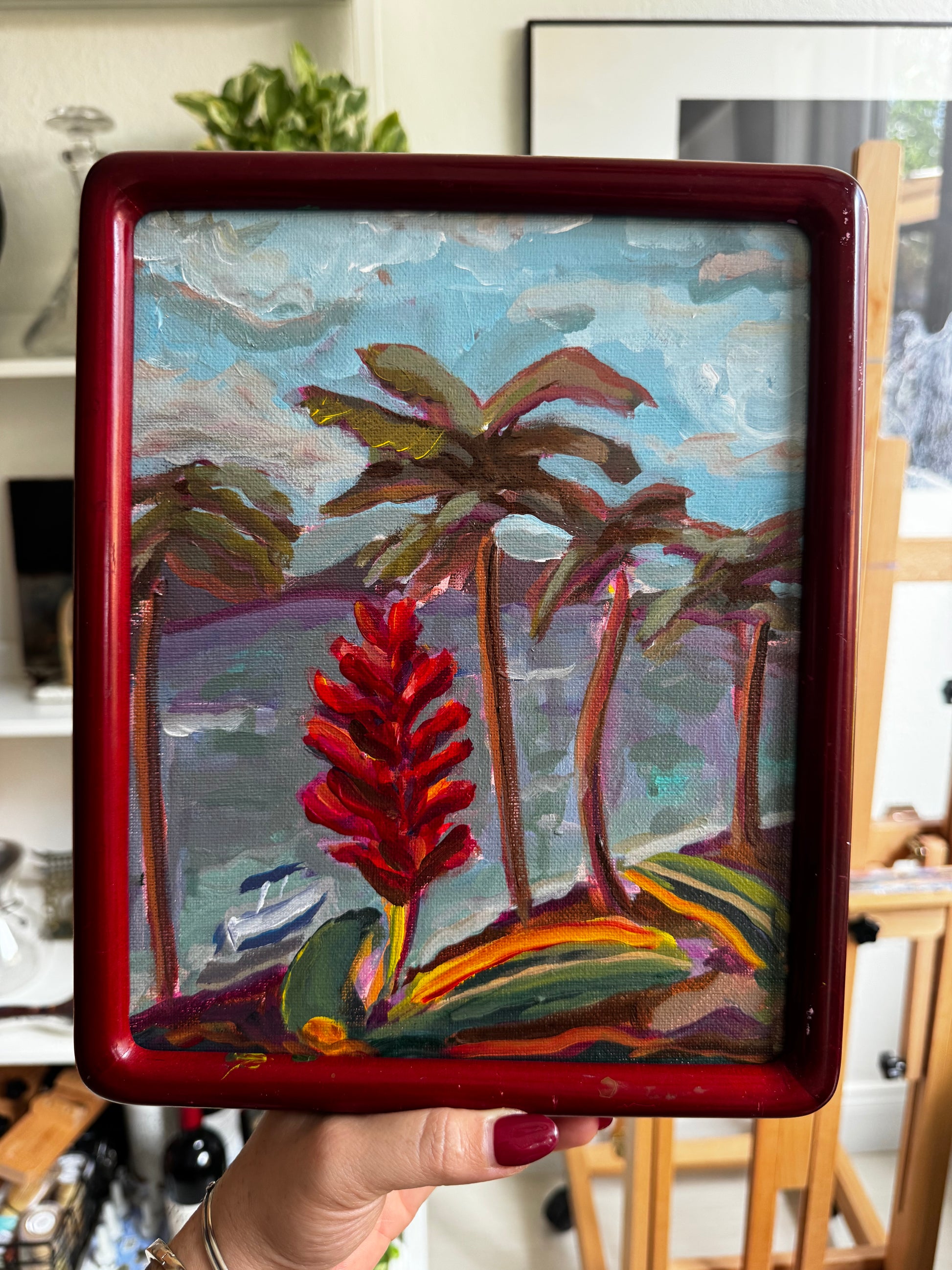 Artistic depiction of flowers in a red frame held by a hand.