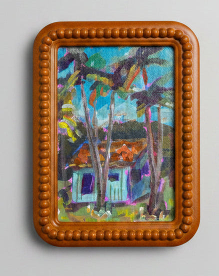 Small painting of a house in a forest with a brown frame on a light gray background
