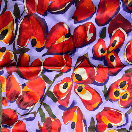 A close-up of a patterned fabric featuring large, abstract red and orange floral shapes with black and white details on a light purple background.