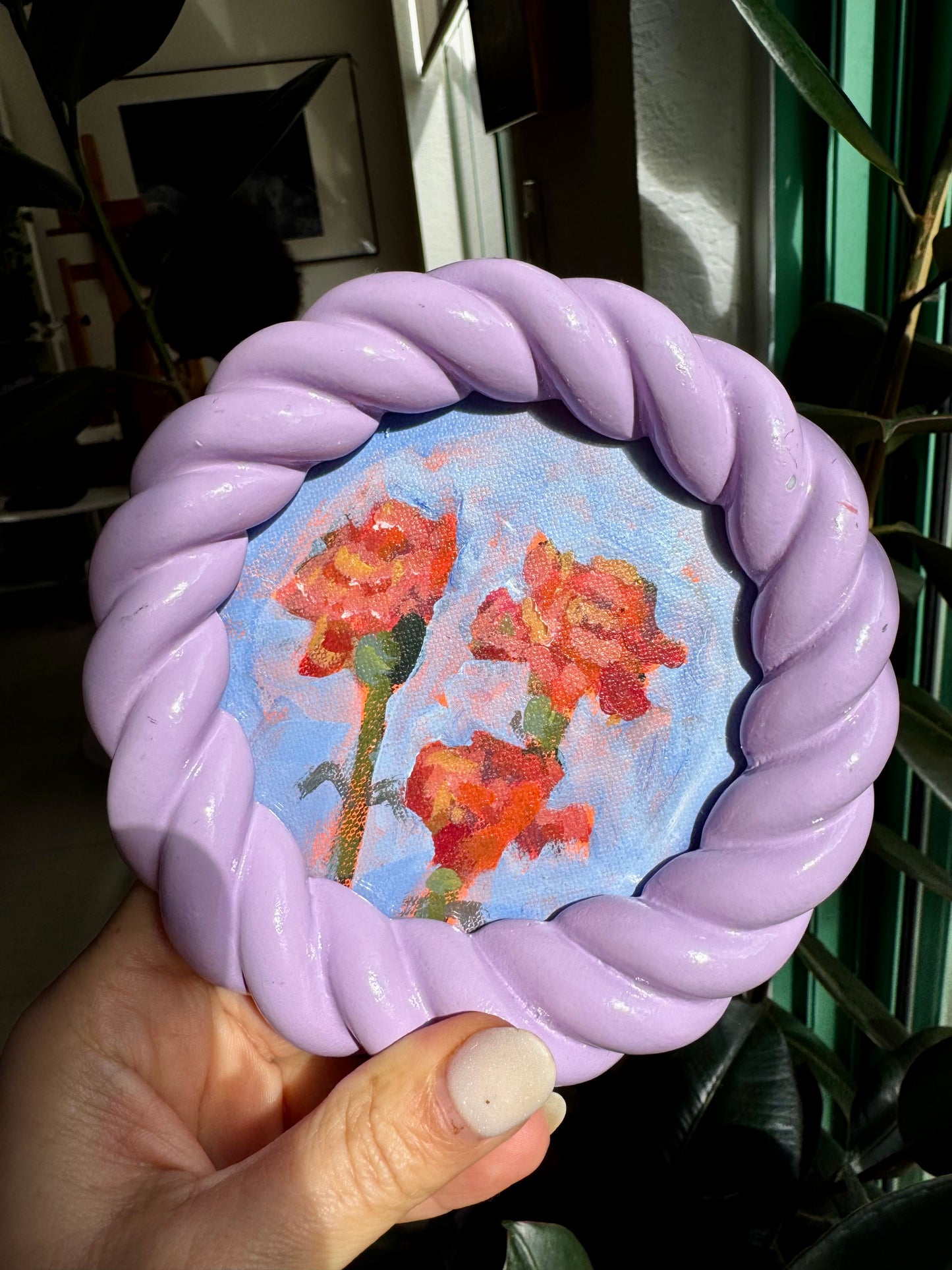 Hand holding a round object with a floral design inside a purple frame.