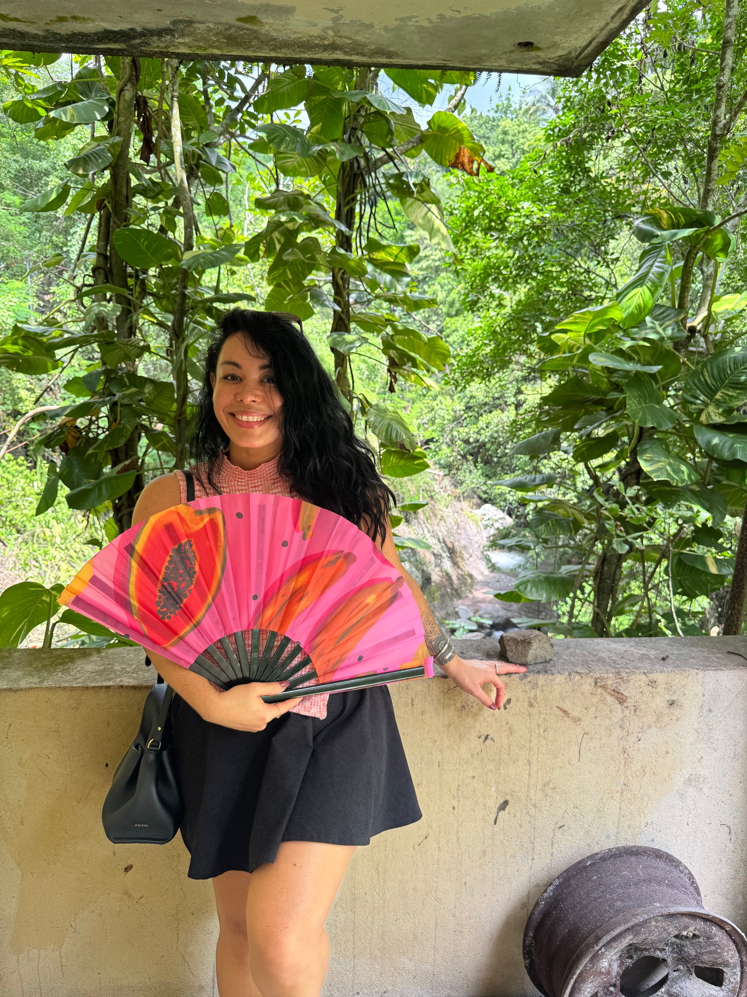 Person holding a pink fan with floral design under a tree