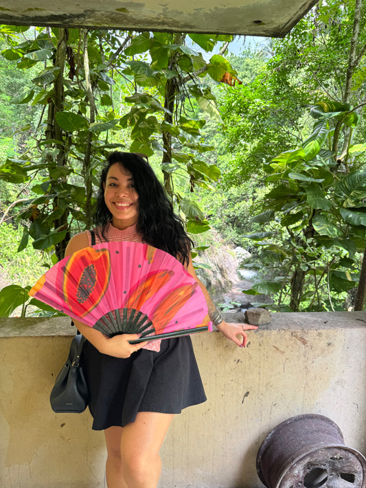 Person holding a pink fan with floral design under a tree