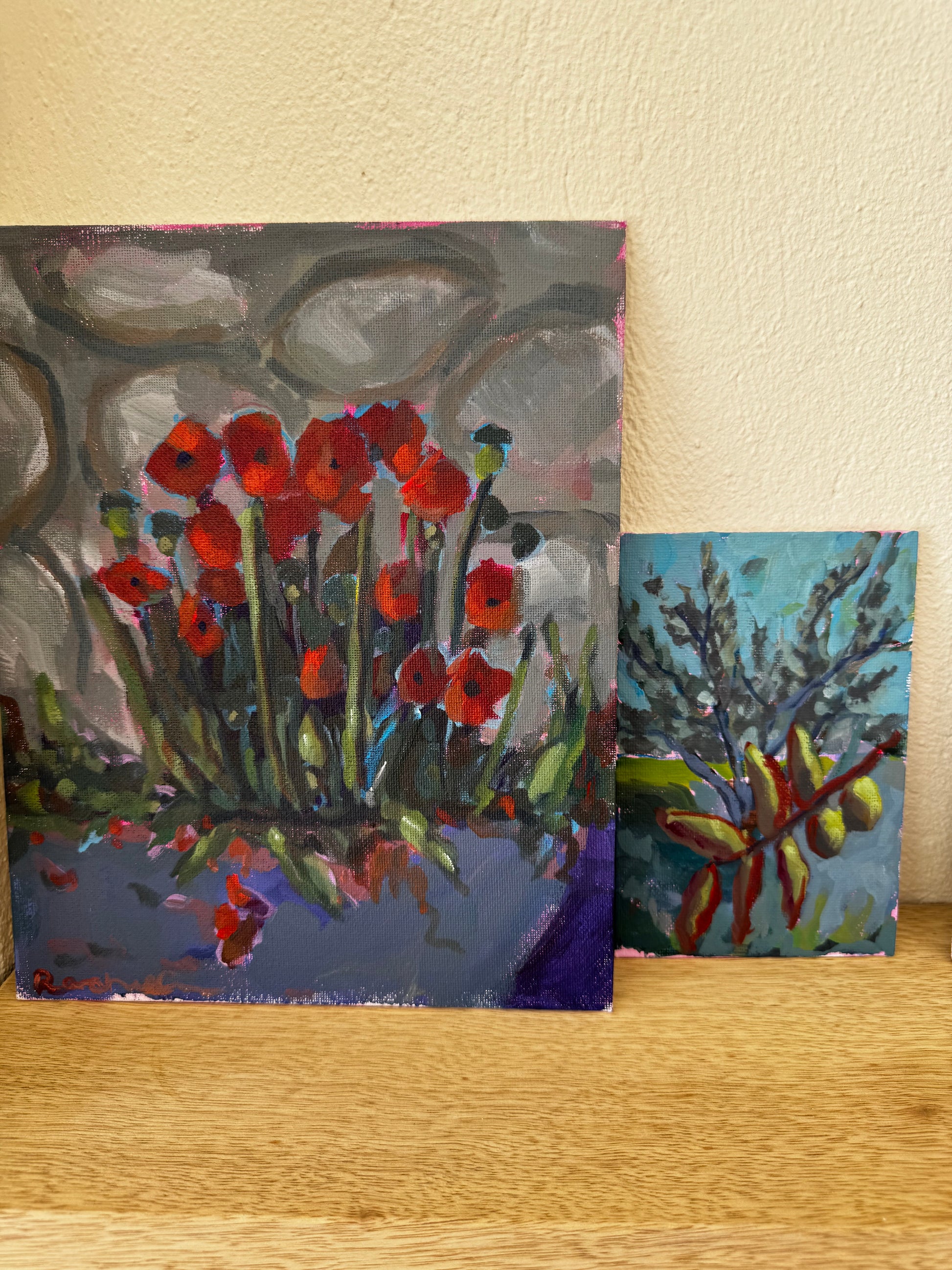 Two small artworks on a wooden surface with a neutral background