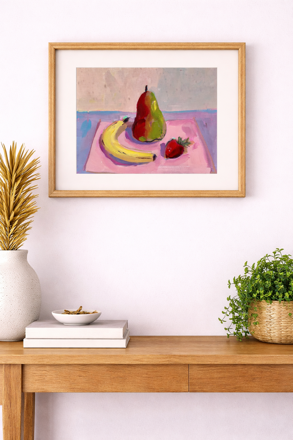 Framed still life painting of fruit on a wall above a wooden console table with decor items.