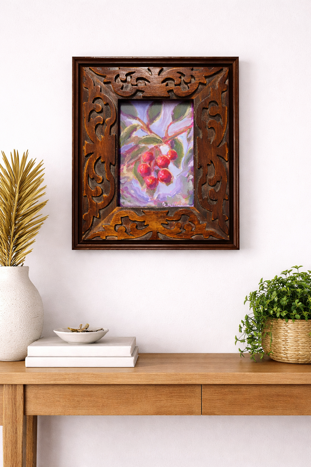 Decorative wooden frame with a painting of berries on a wall above a wooden console table.
