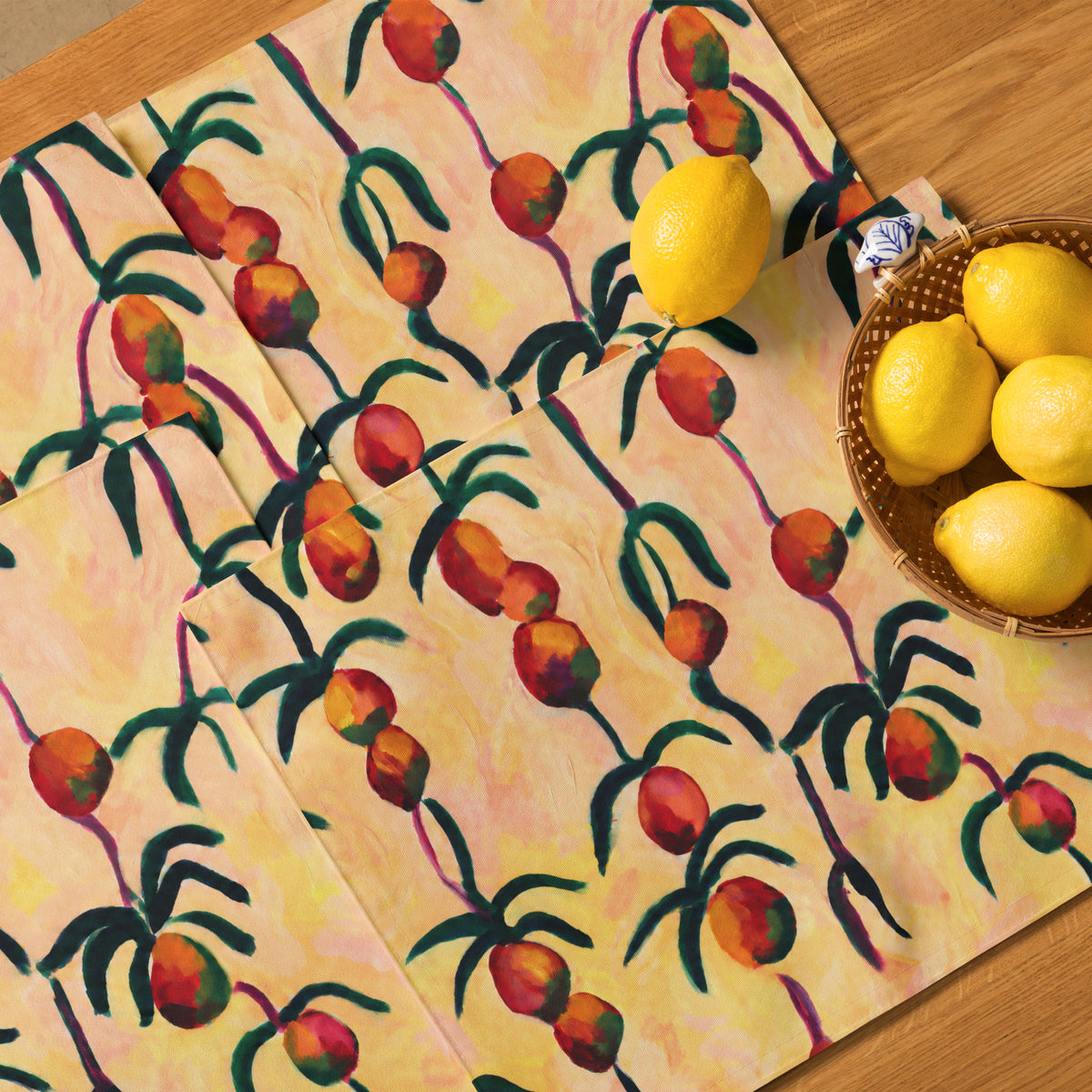 A set of rectangular placemats with a colorful tropical pattern of lemons and palm trees, styled on a wooden table next to a basket of lemons.