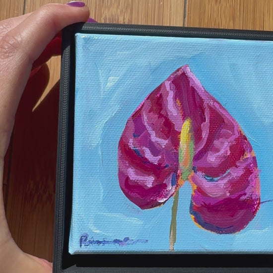Video of Artistic depiction of a pink flower with a blue background. Hand moving it around against a wood background. 