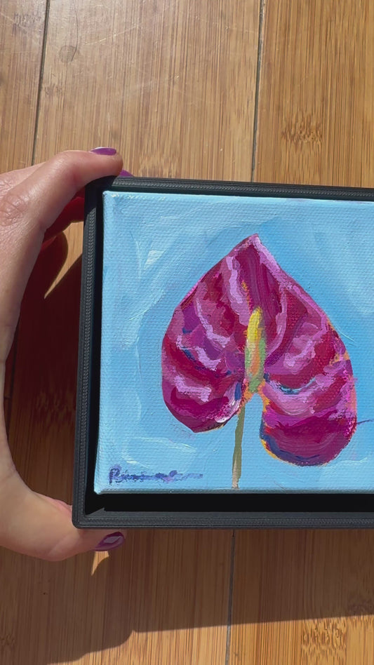 Video of Artistic depiction of a pink flower with a blue background. Hand moving it around against a wood background. 