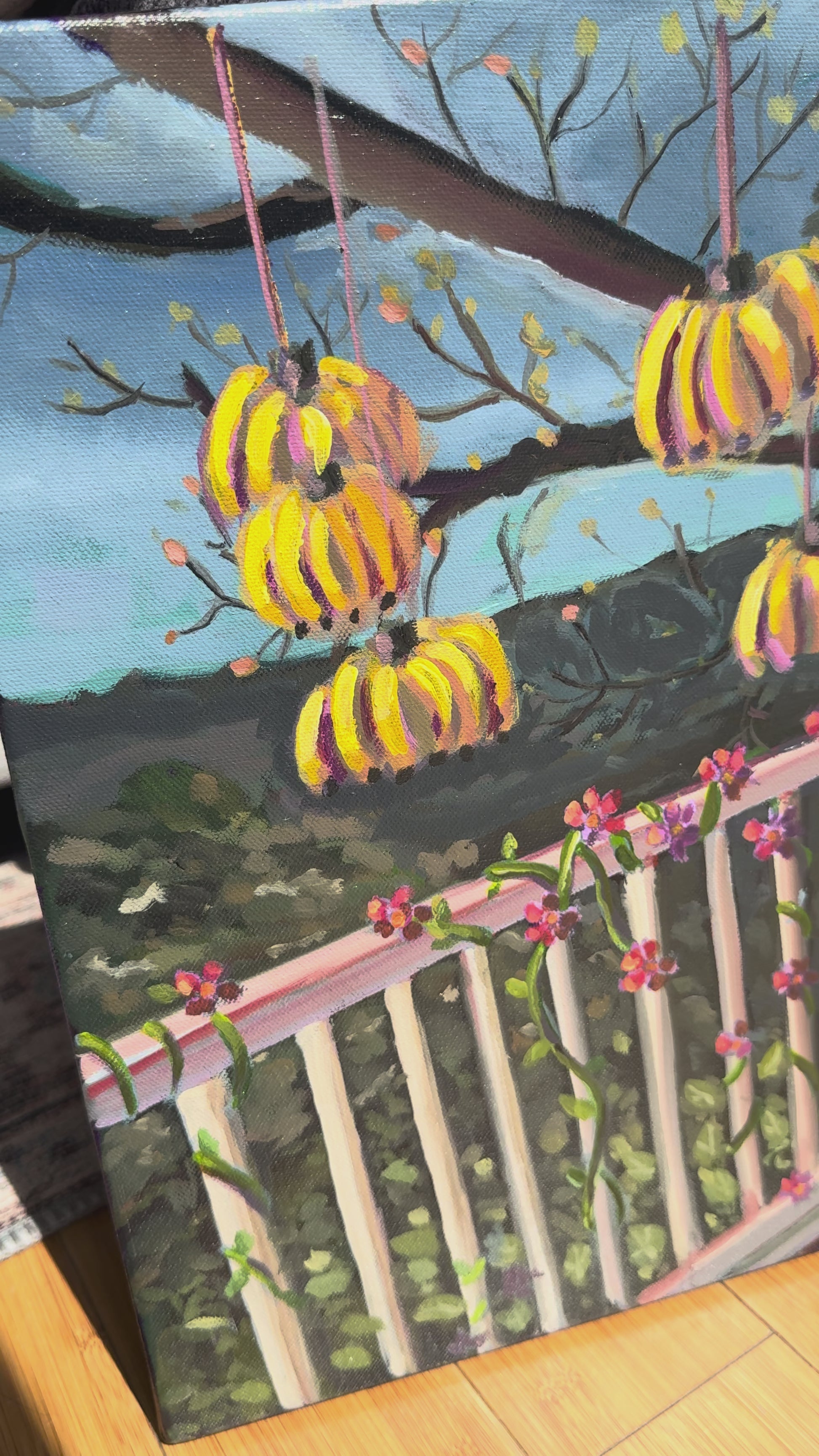 Video of painting with bananas and pineapple hanging on a balcony overlooking mountains. 