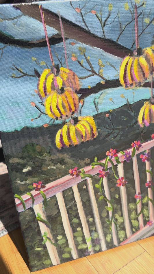 Video of painting with bananas and pineapple hanging on a balcony overlooking mountains. 