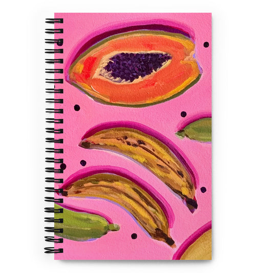A spiral notebook with a pink cover featuring artistic depictions of fruits, including a banana and a papaya.